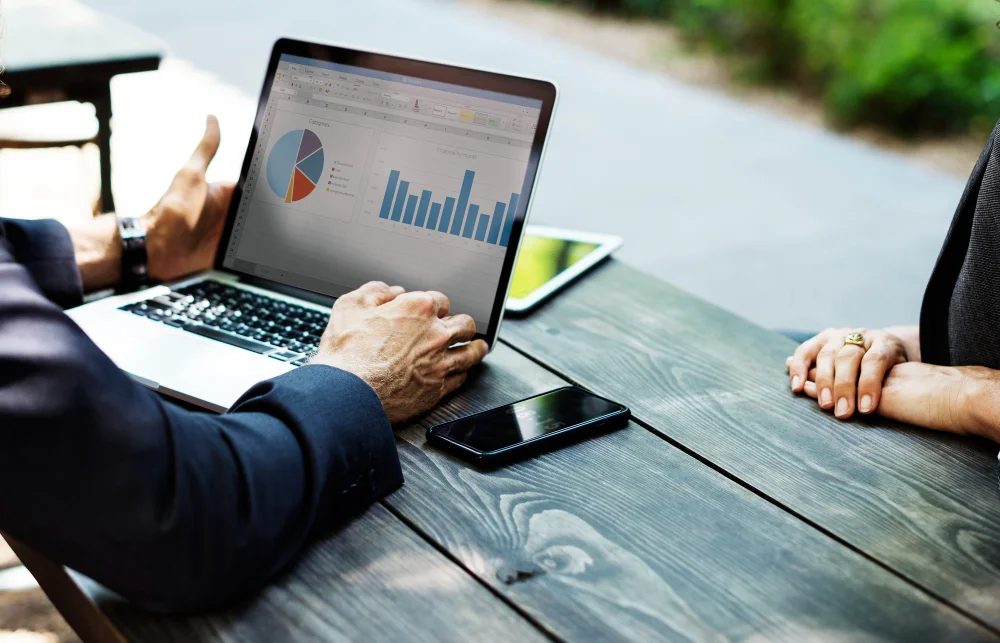Two business professionals reviewing backlink audit analytics on laptop showing pie chart and bar graph data, discussing link building strategy for contractor SEO ranking analysis